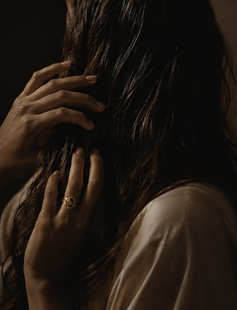Dark hair caught in warm light, hands lifted to the lengths