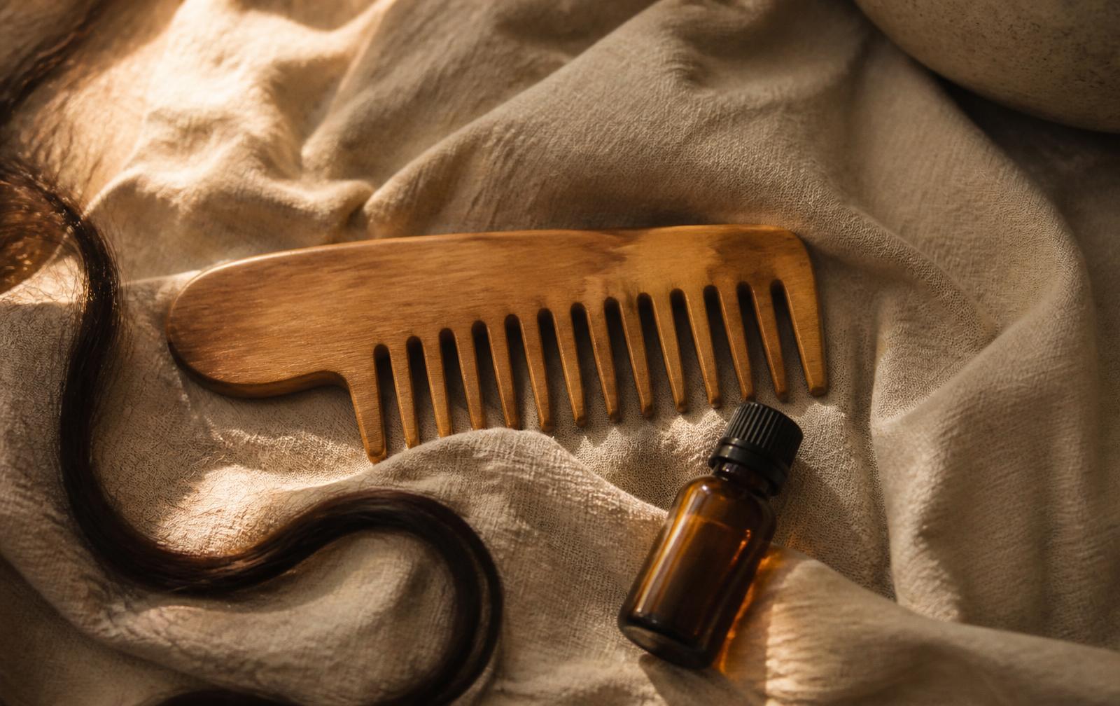 Wooden comb, linen cloth and an amber oil bottle in warm light